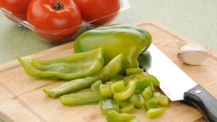 Diced green pepper on a cutting board with a container of tomatoes in the background