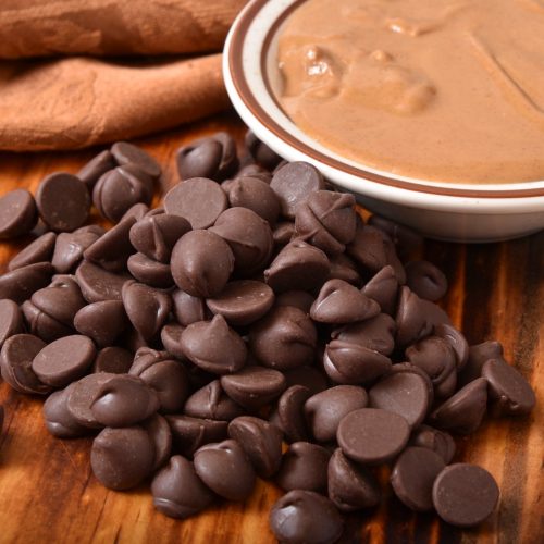 Closeup of dark chocolate chips with a bowl of peanut butter