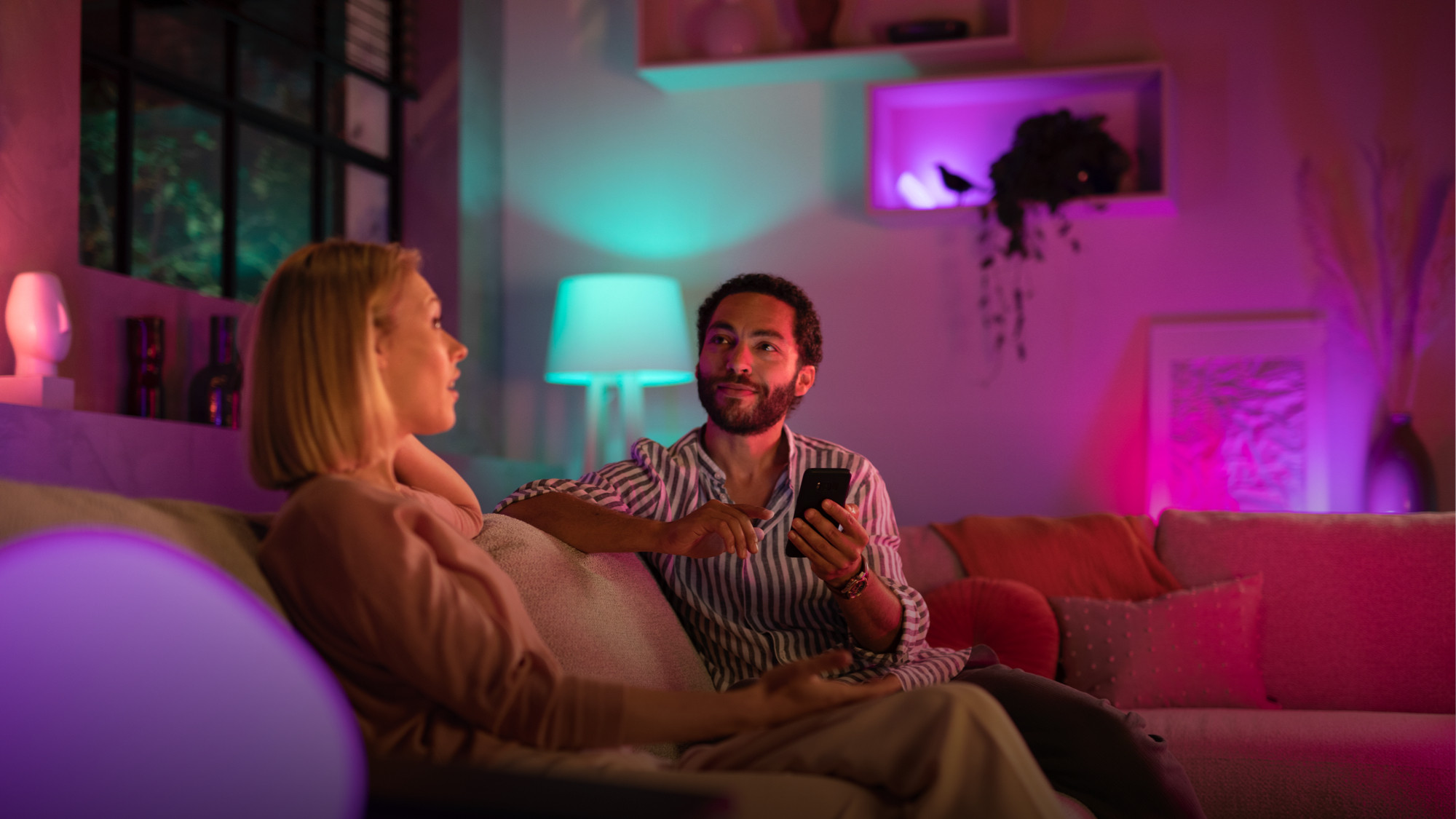 Philips Hue smart lights illuminate a room as two people chat